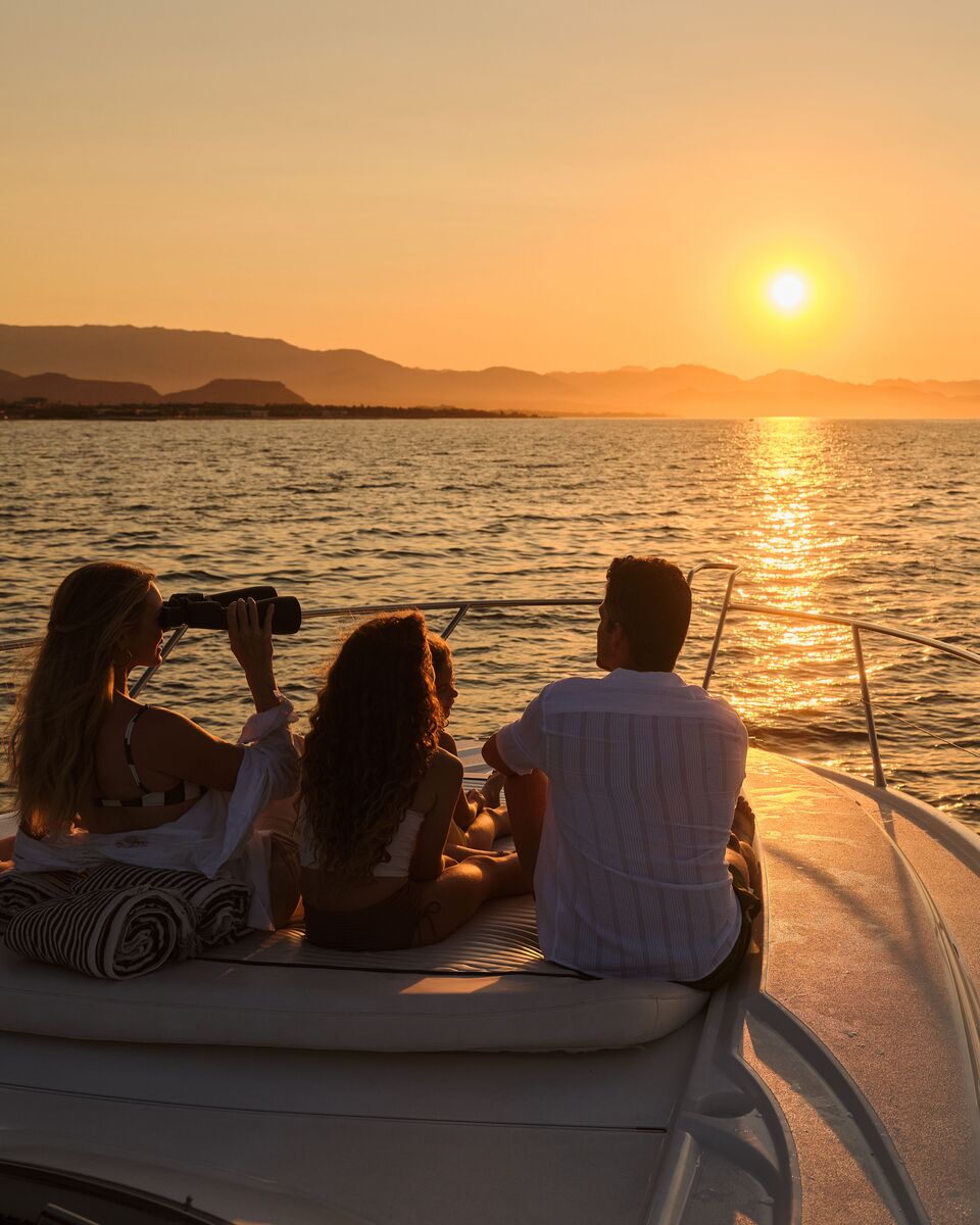 Guests on the bow of a boat watching the sun set over the Sea of Cortez